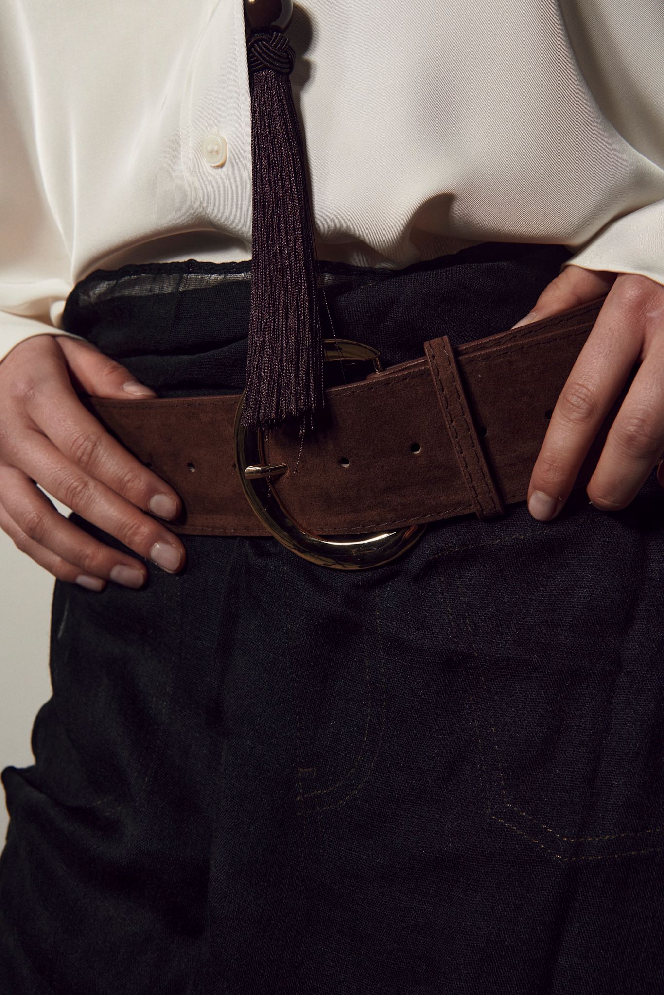 Person wearing a white shirt and dark pants with a brown belt.